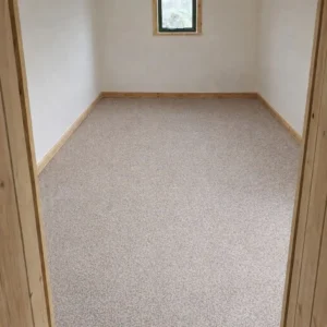 Shepherd’s hut interior with beige carpet flooring and timber skirting in a finished room layout
