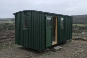 Shepherd’s hut exterior with dark green painted timber cladding, matching door and windows, set in a Highland landscape