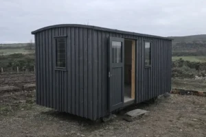 Shepherd’s hut exterior with dark grey painted timber cladding, matching door and windows, set in a Highland landscape