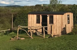 Shepherd’s hut exterior with timber cladding, black door and rural hillside setting