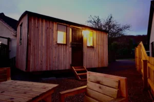Shepherd’s hut exterior at dusk with warm interior lighting and timber cladding