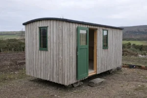 Shepherd’s hut exterior with Scottish larch cladding, green timber door and windows, set in a Highland landscape