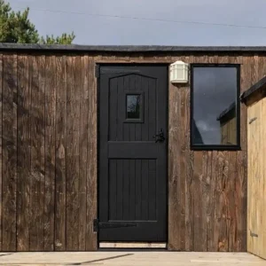 Shepherd’s hut exterior with weathered timber cladding, black door and matching window frames