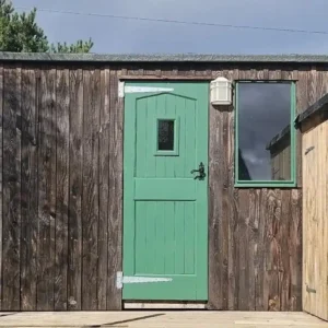 Shepherd’s hut exterior with weathered timber cladding, green door and matching window frames