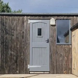 Shepherd’s hut exterior with weathered timber cladding, grey door and matching window frames