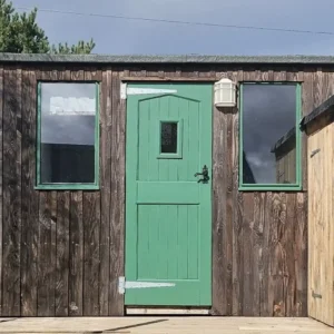 Shepherd’s hut exterior with weathered timber cladding, green door and matching window frames